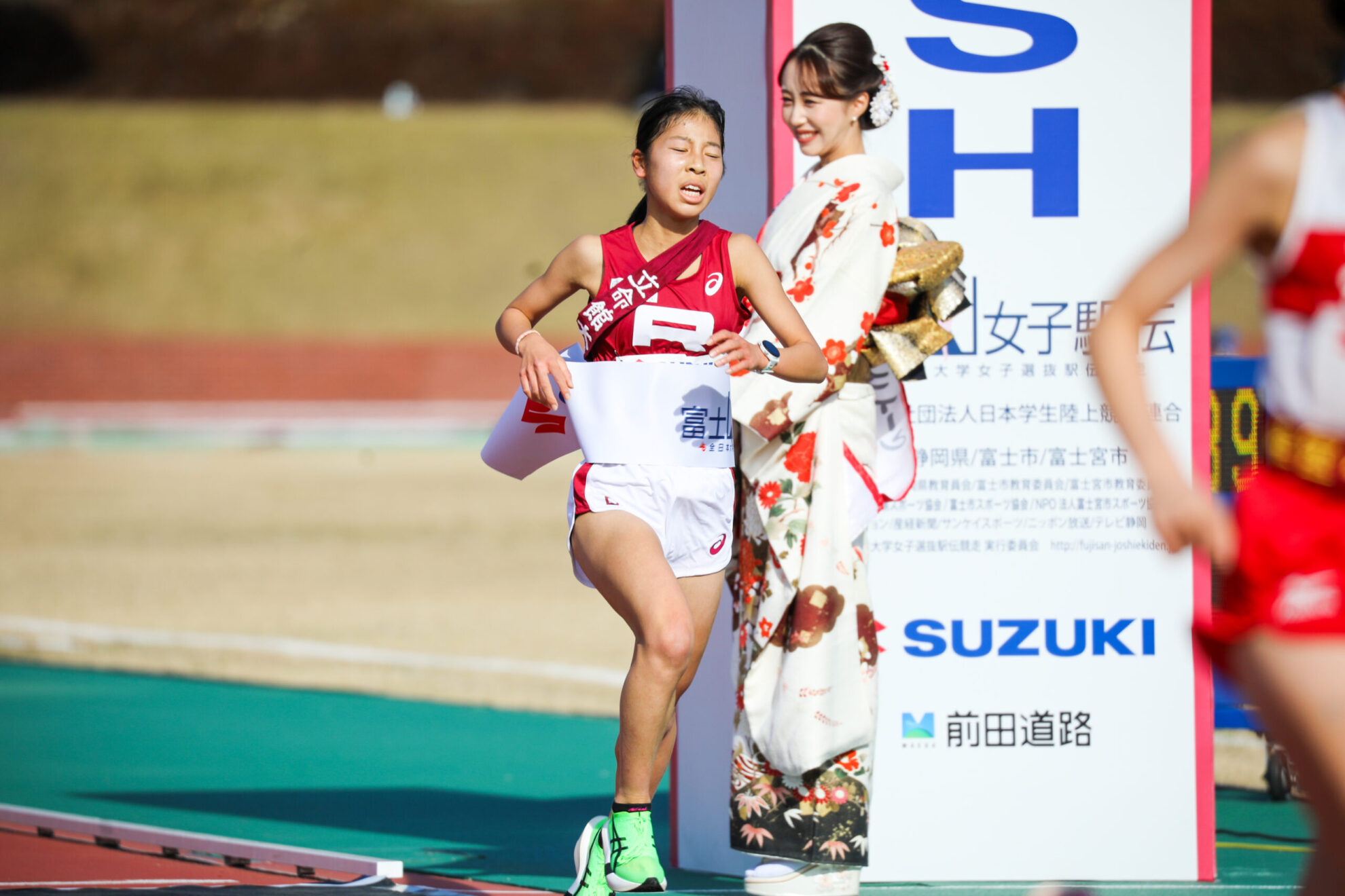 たすきを掛け、着物を着た女性が持つゴールテープを着る弓木。
